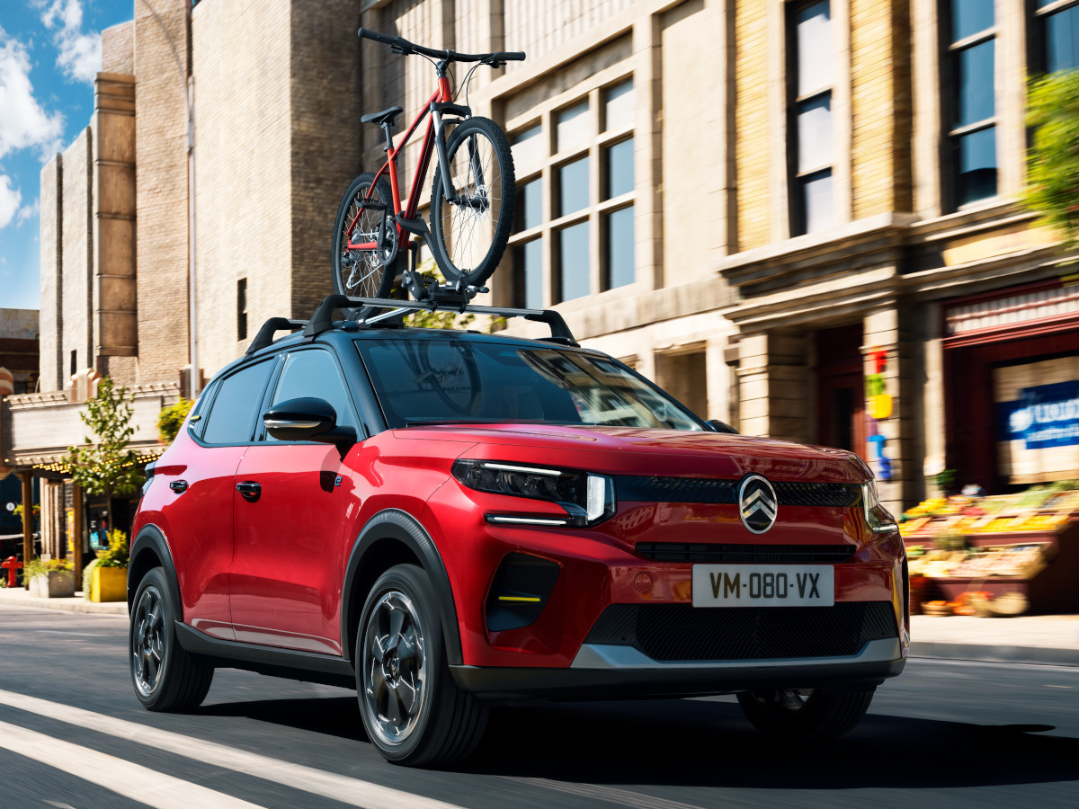 Roter Citroën mit Fahrradträger fährt durch die Stadt bei Sonnenschein
